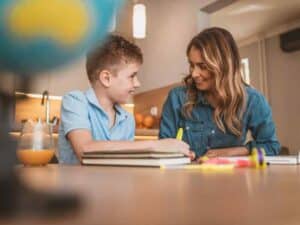 Mother helping her son with homework at a kitchen table, with books and a yellow highlighter nearby.
